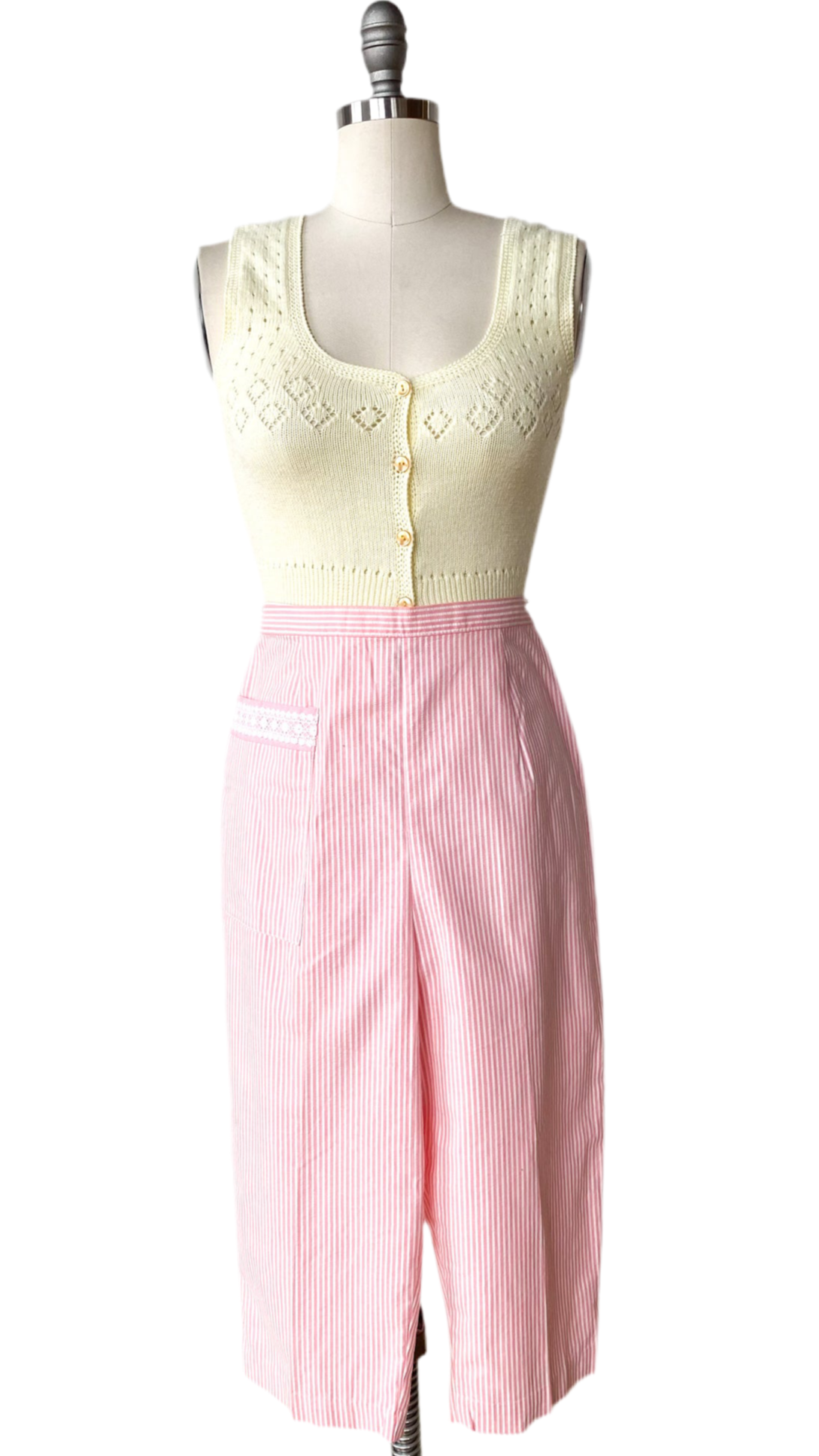 Mannequin wearing a cream sleeveless top with lace details and pink striped pants on a white background