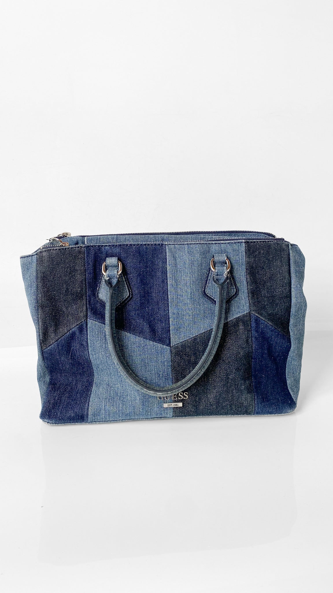 A blue patchwork denim tote bag with dual top handles and a top zipper closure, displayed on a clean white background.