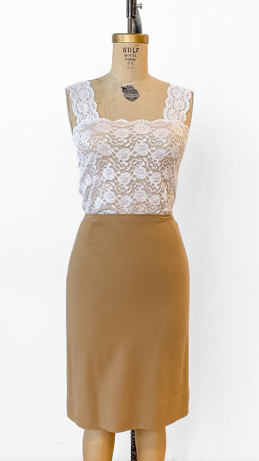 Mannequin wearing a white lace top and brown skirt on a wooden floor.