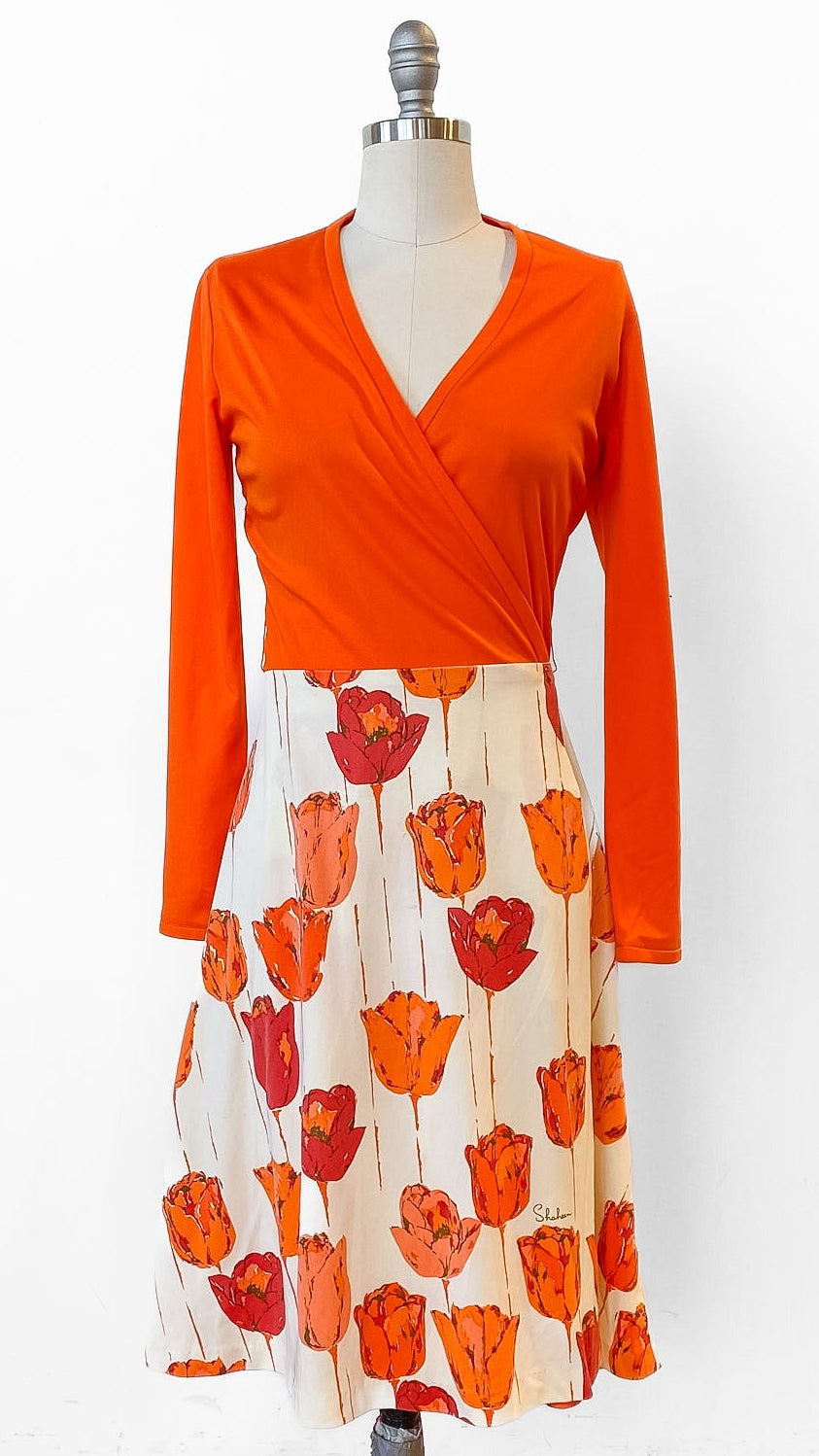Mannequin wearing an orange top and floral skirt on a wooden floor with white background
