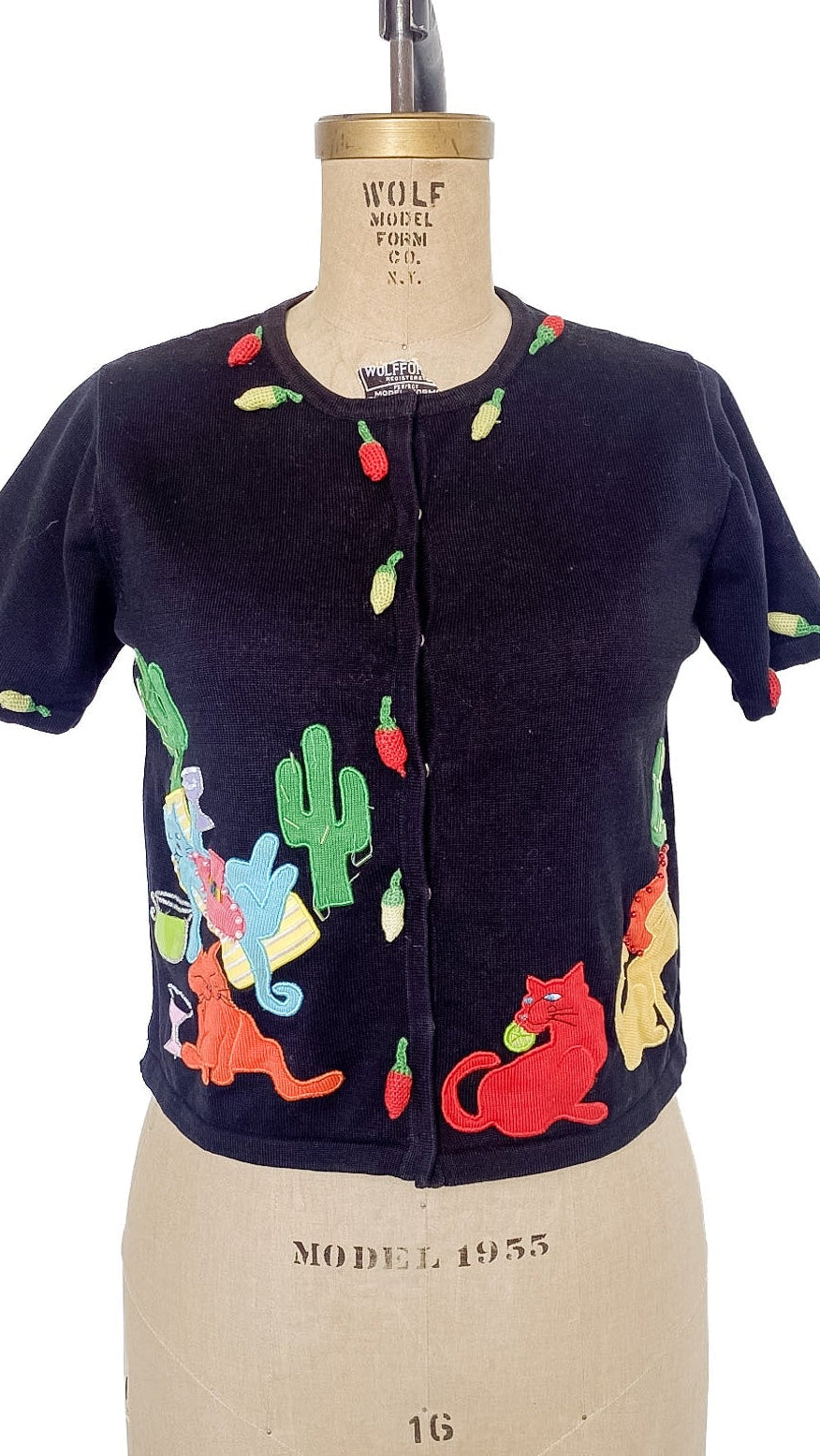 Black cardigan with colorful cat pattern on a mannequin against a white background