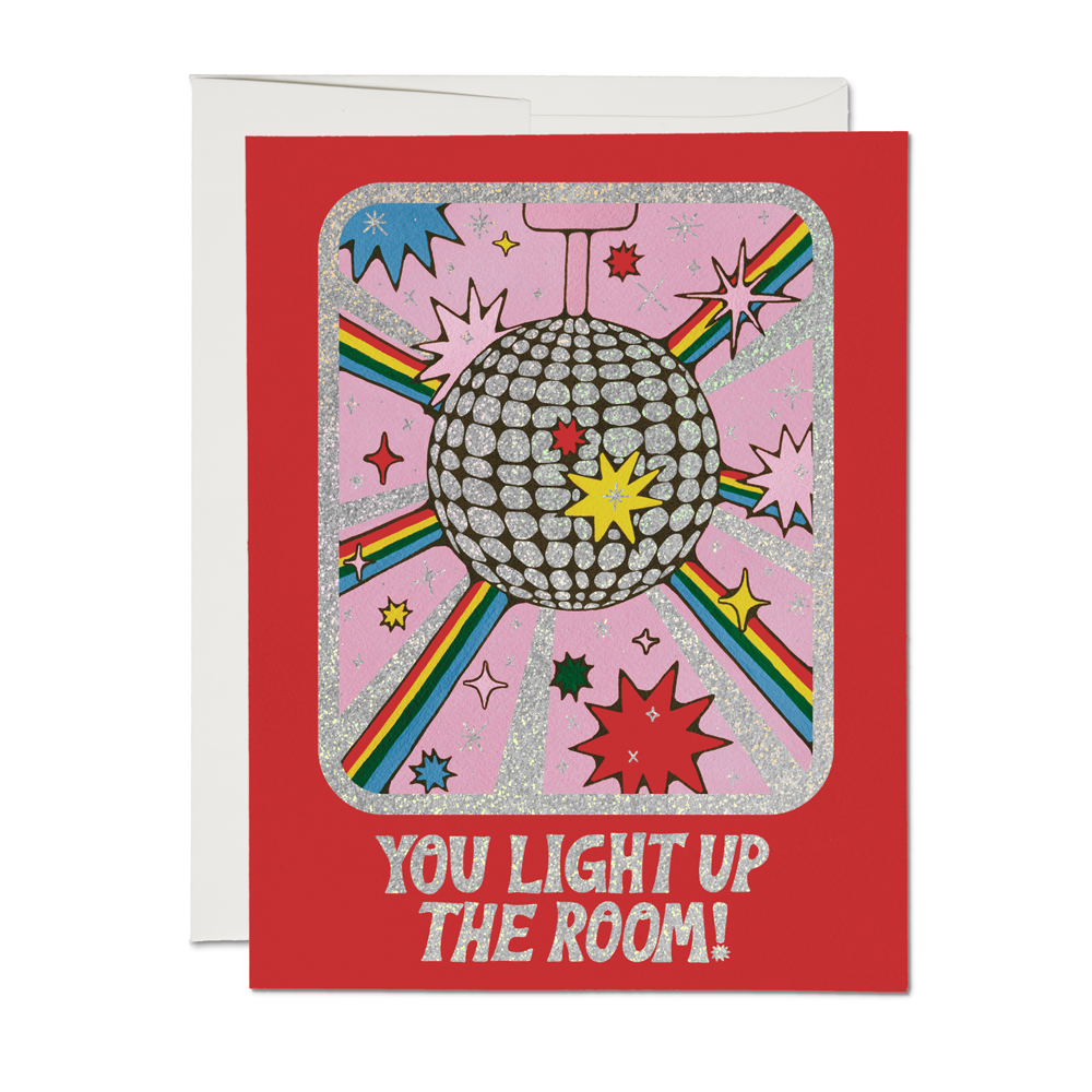 A greeting card with an illustrated disco ball and colorful accents, featuring the text 'YOU LIGHT UP THE ROOM!' by Krista Perry.