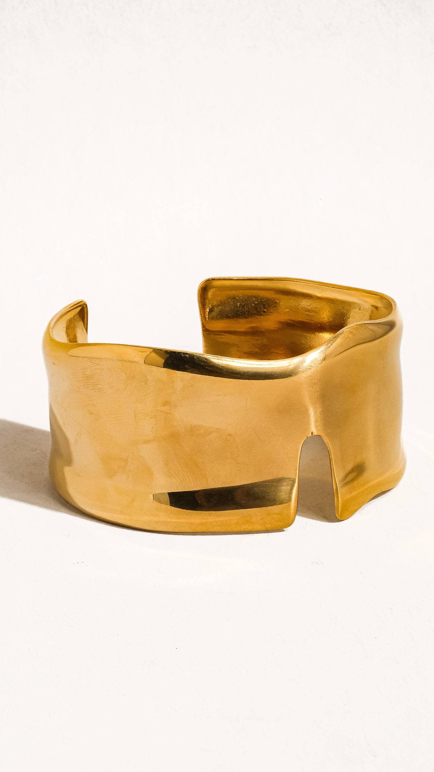 A gold-colored bangle bracelet with an abstract design, displayed against a white background.