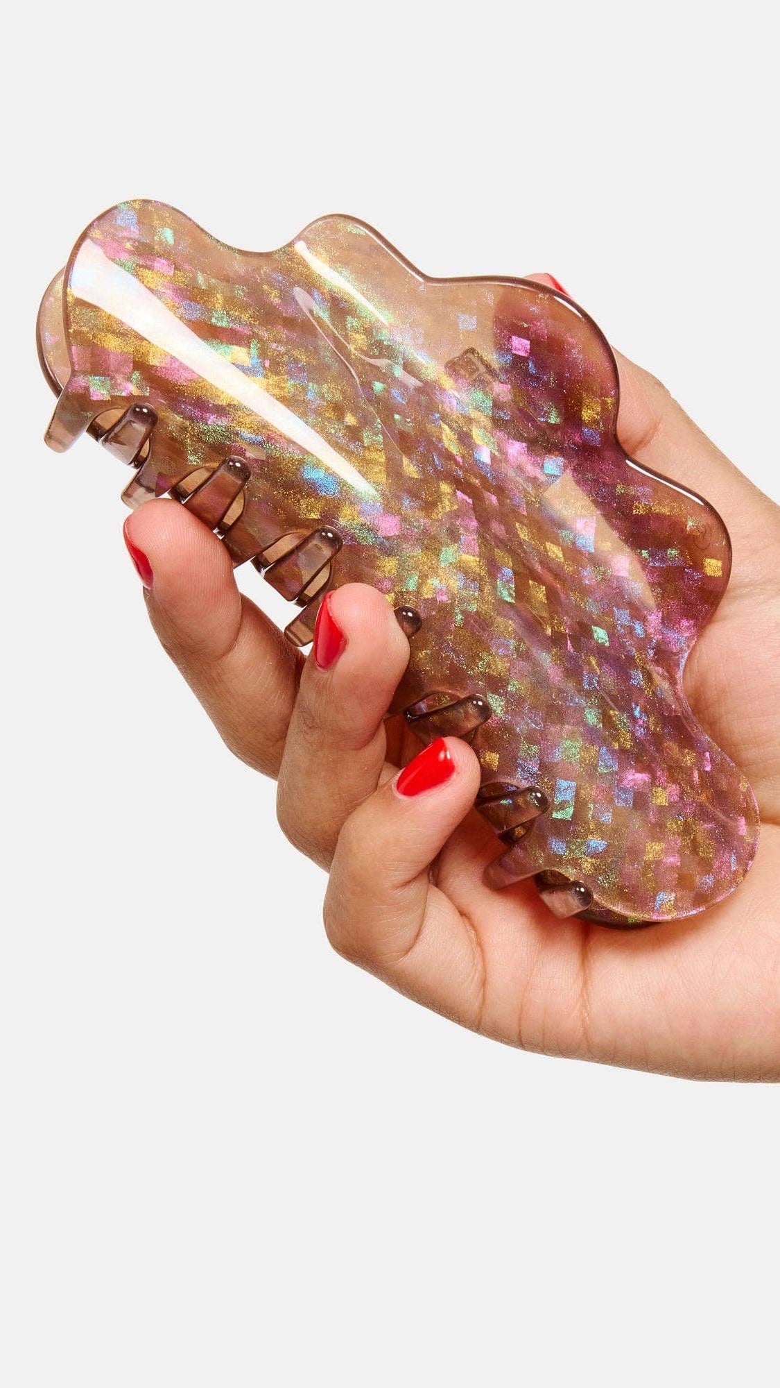 Hand holding a large, iridescent hair clip against a white background