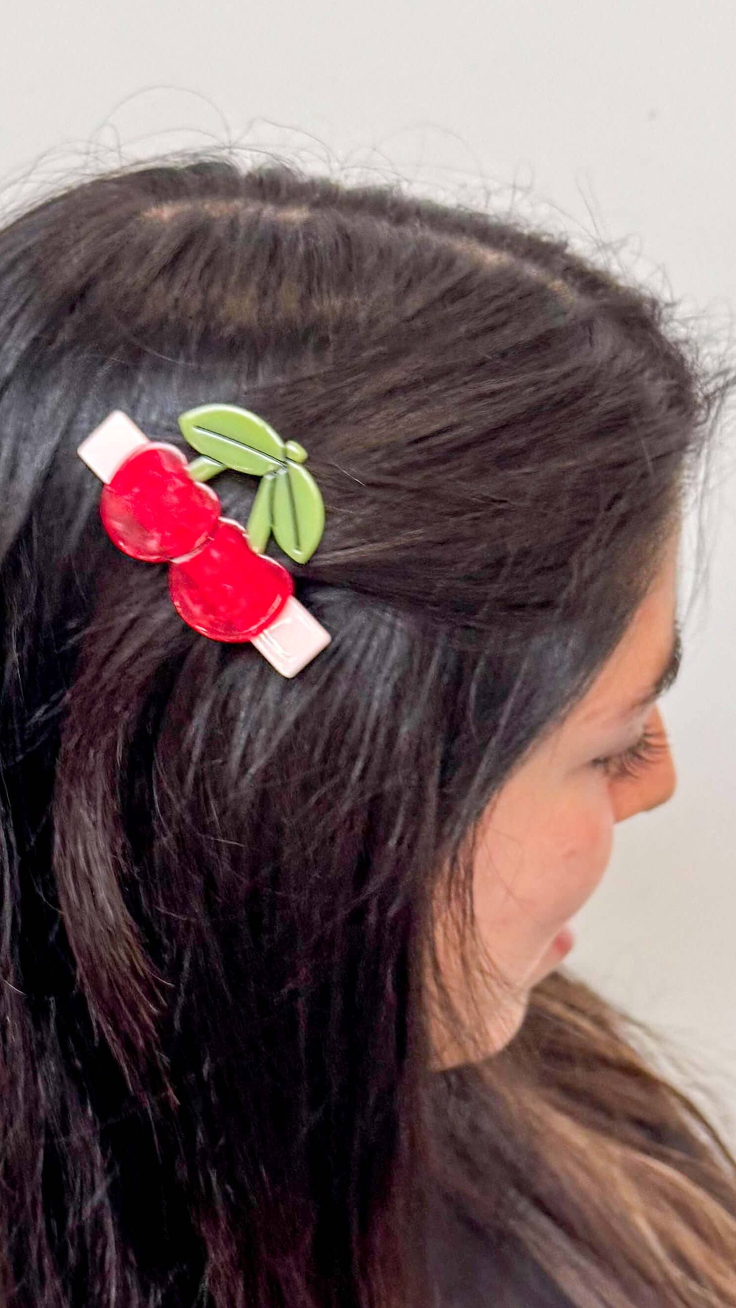 Person wearing a hair clip with red berries and green leaves on a plain background