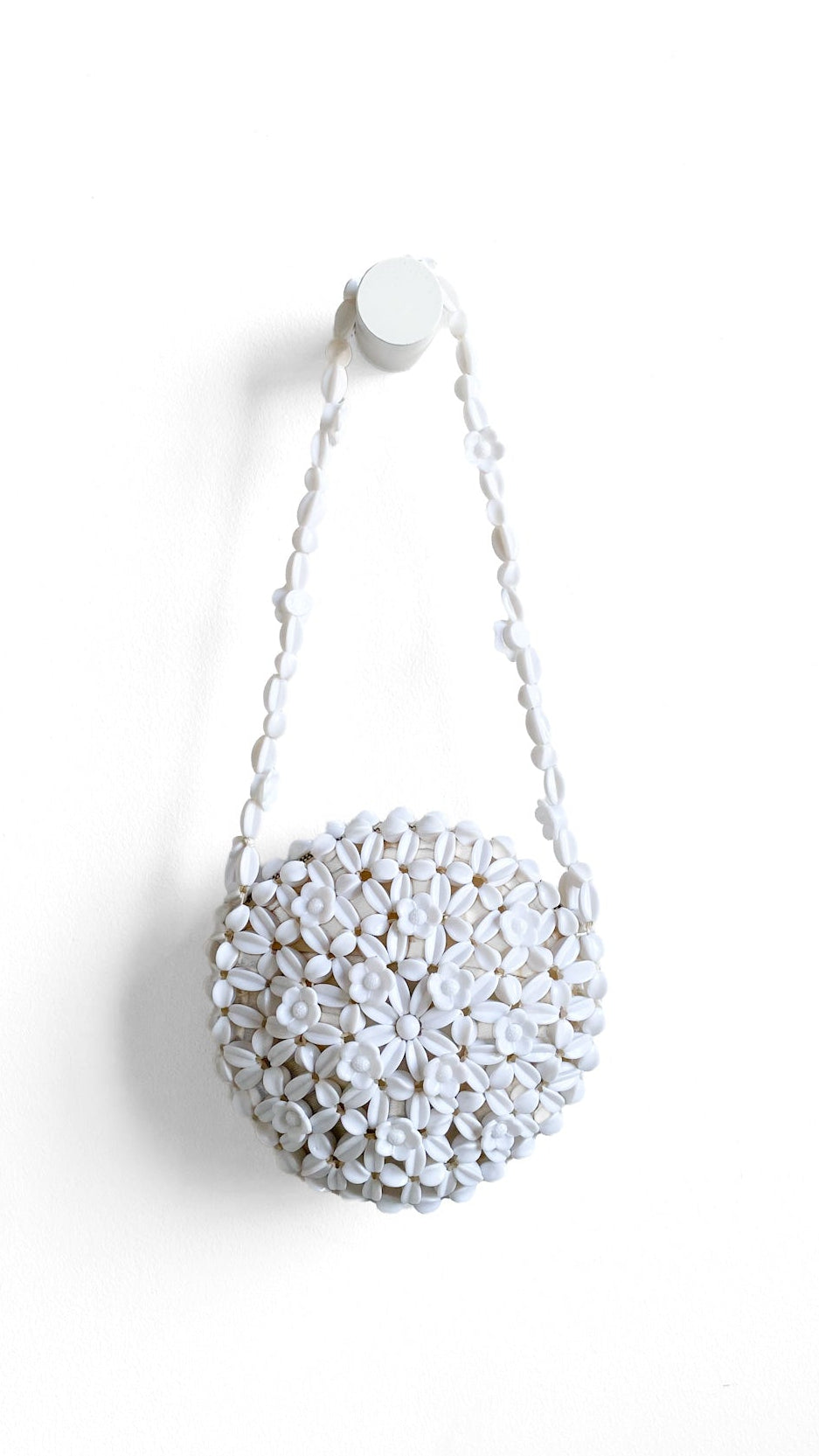 A white beaded spherical shoulder bag with a matching beaded chain strap, hanging from a white wall hook against a plain white background.
