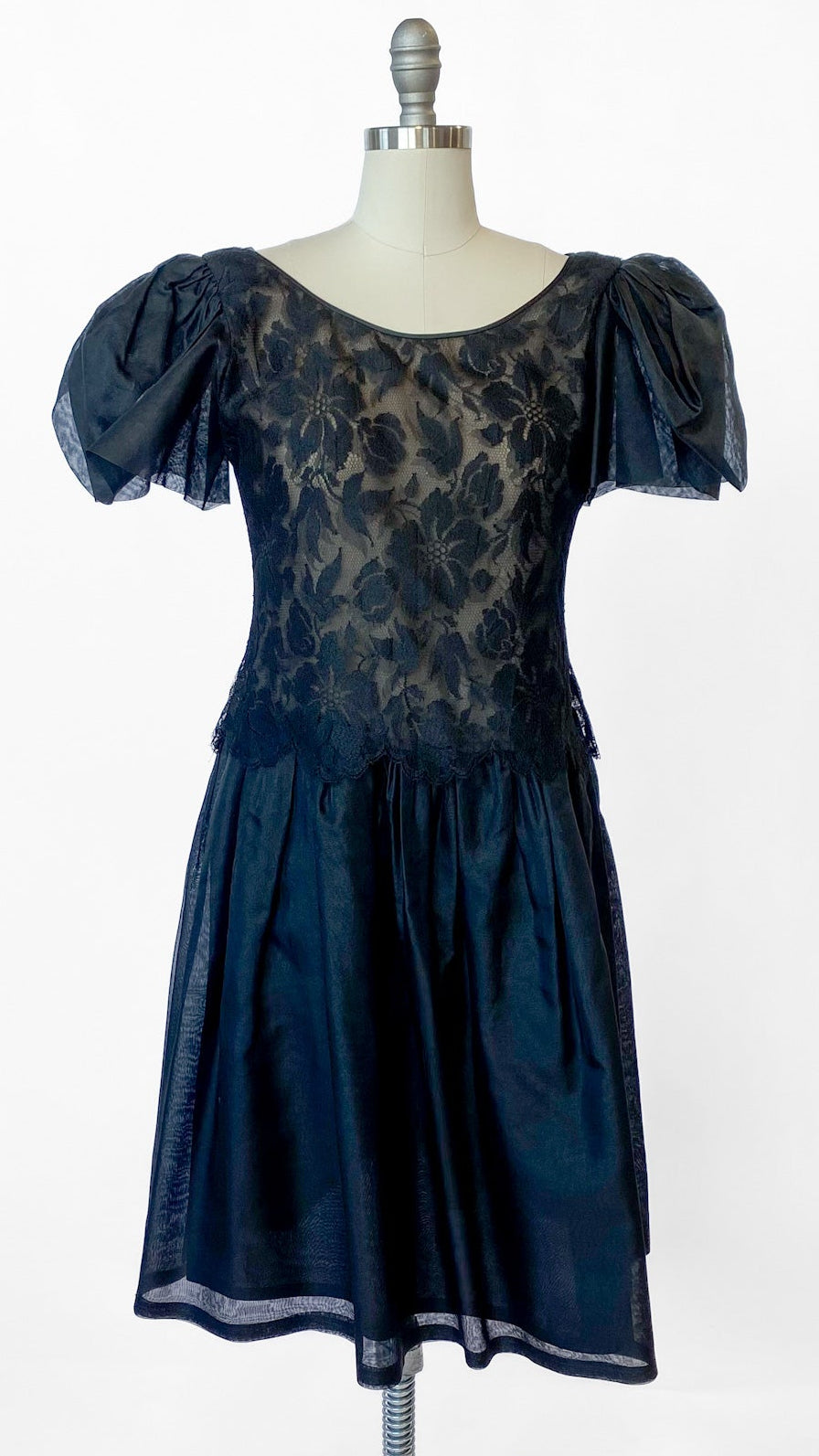 Black dress with floral lace pattern on a mannequin against a white background
