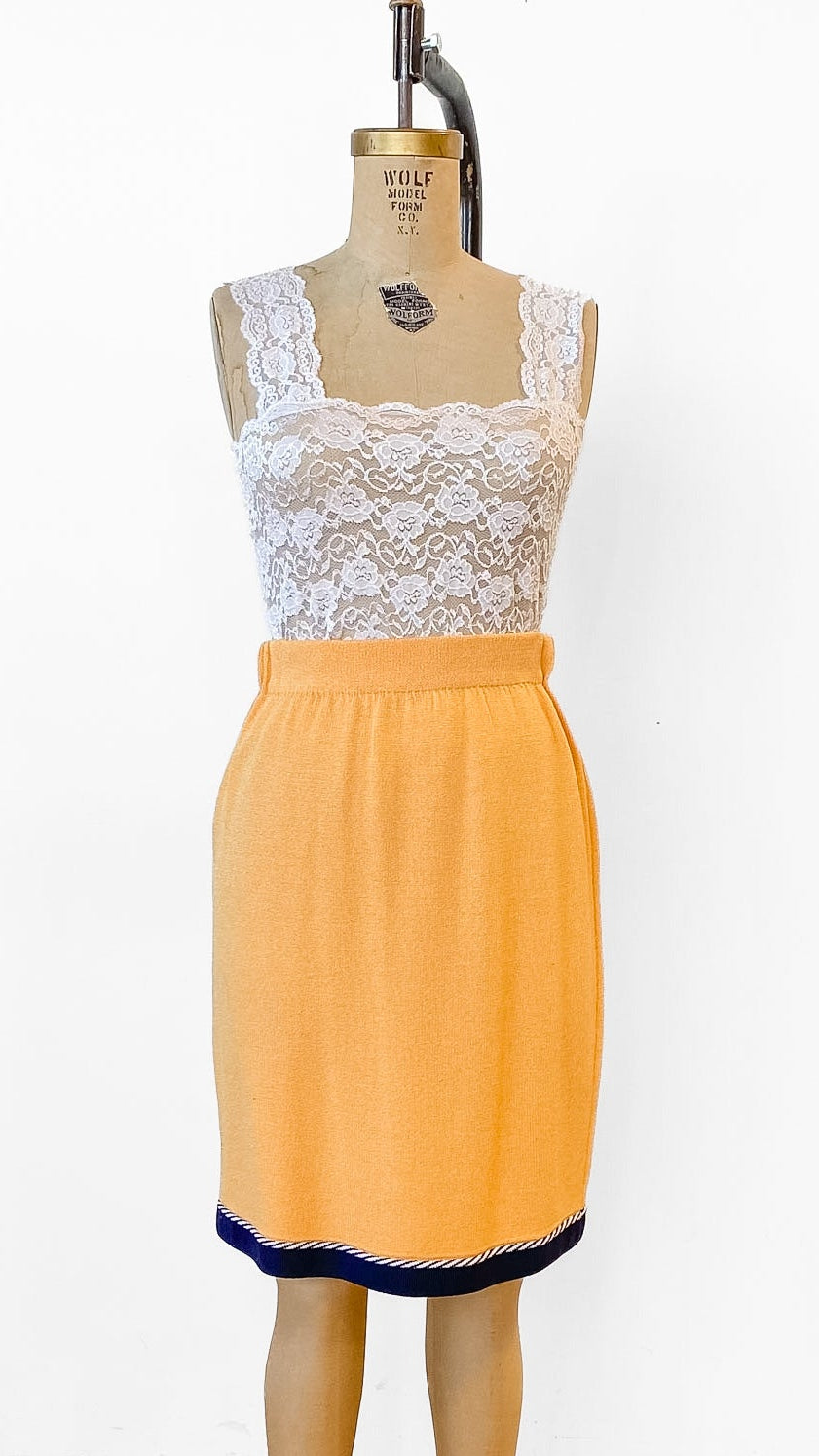 Mannequin wearing a white lace top and orange skirt on a wooden floor.