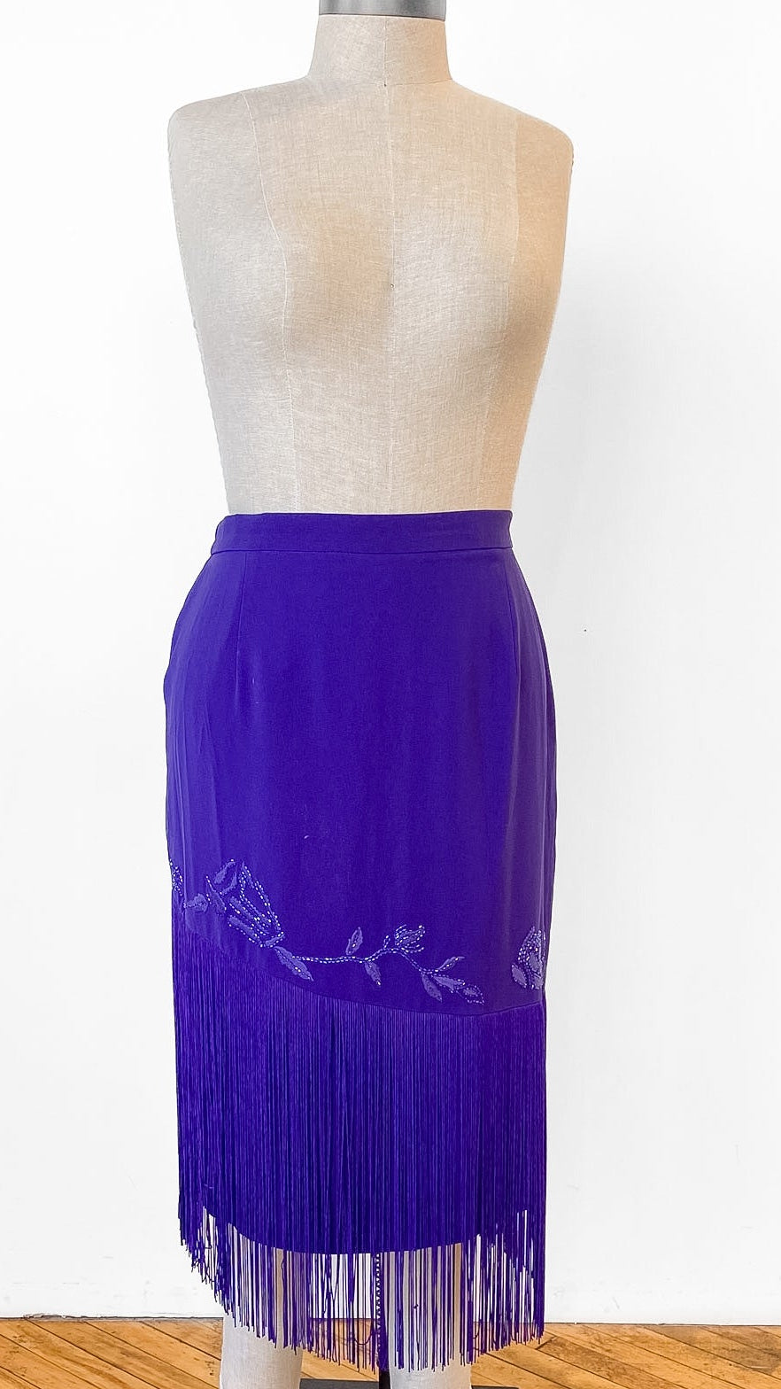Mannequin wearing a purple fringe skirt on a wooden floor with a white background