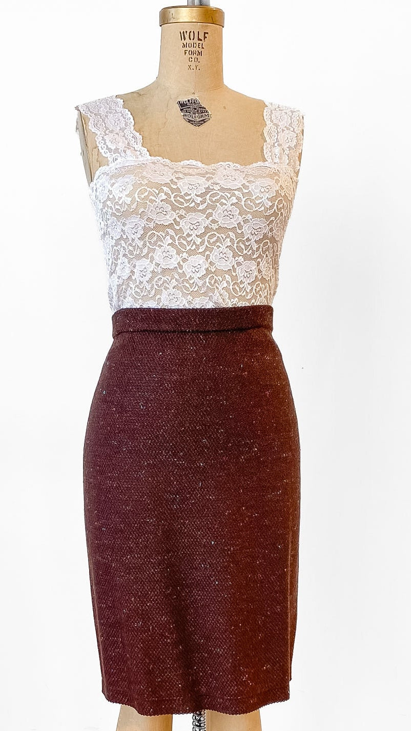 Mannequin wearing a white lace top and brown skirt on a wooden floor.