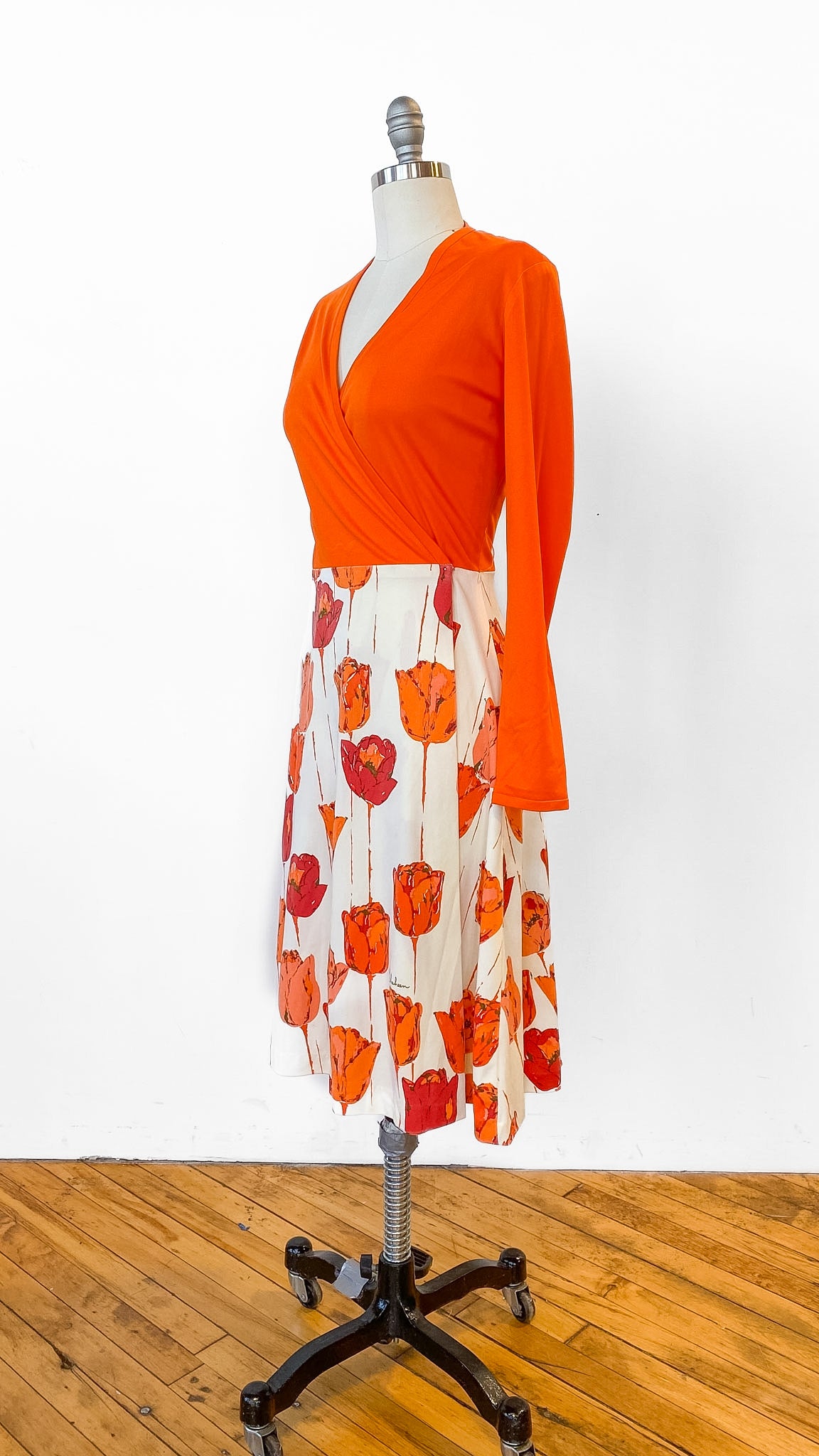 Mannequin wearing an orange top and floral skirt on a wooden floor with white background
