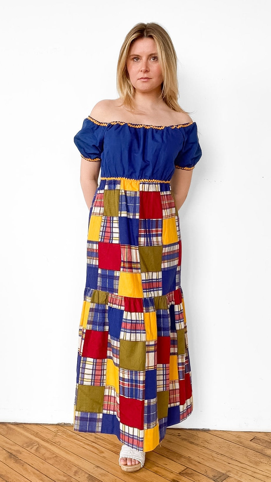 Woman wearing a colorful patchwork dress with a blue top against a white background