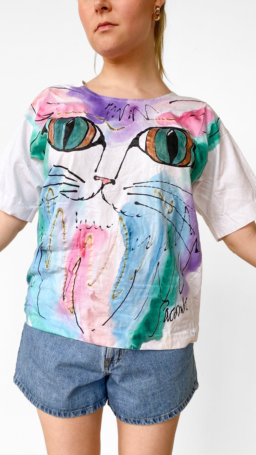 Person wearing a colorful cat-themed t-shirt and denim shorts on a plain background