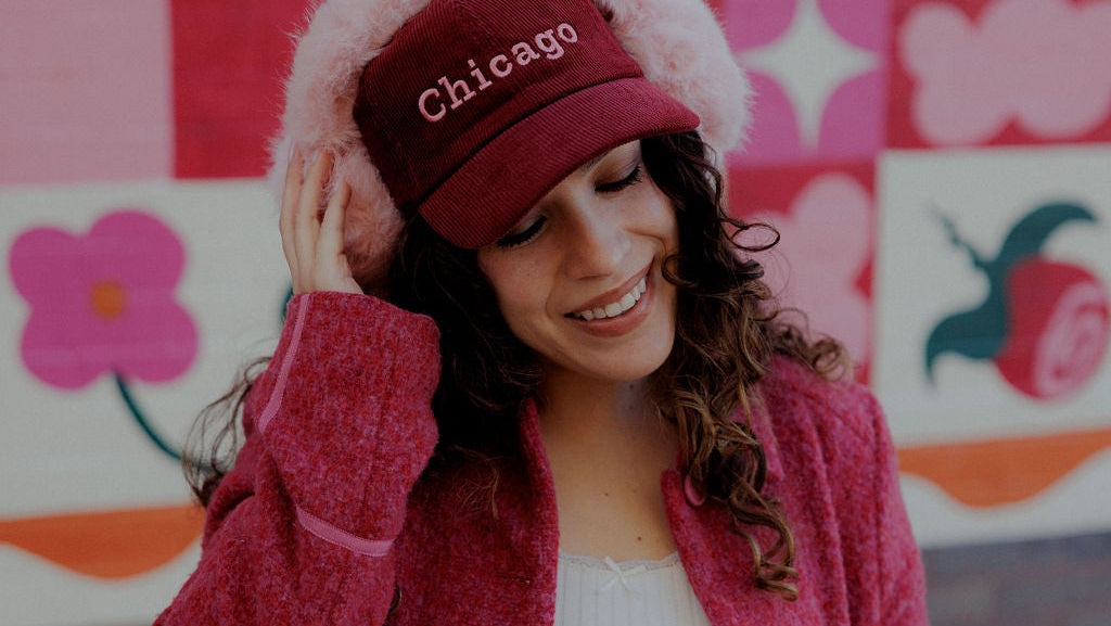 Woman wearing a red coat and 'Chicago' hat in front of a colorful wall.