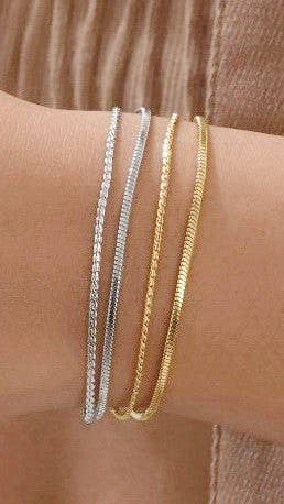 Three gold and silver bracelets on a wrist against a brown background