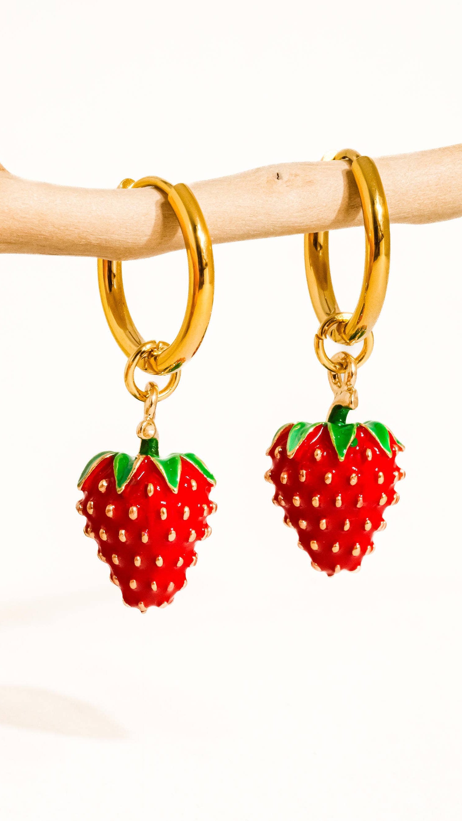 A pair of 18K gold plated stainless steel earrings designed to look like strawberries with a red enamel finish and green accents on a branch.
